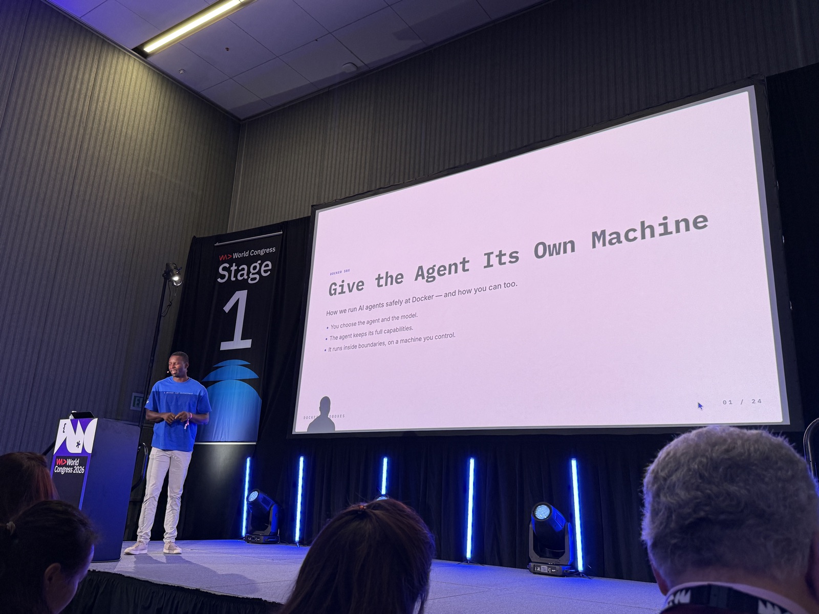 Slide mở đầu Give the Agent Its Own Machine, speaker đứng bên trái Stage 1