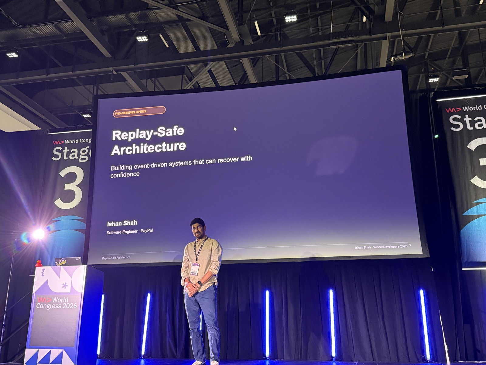 Slide tiêu đề Replay-Safe Architecture, Ishan Shah đứng trên sân khấu Stage 3